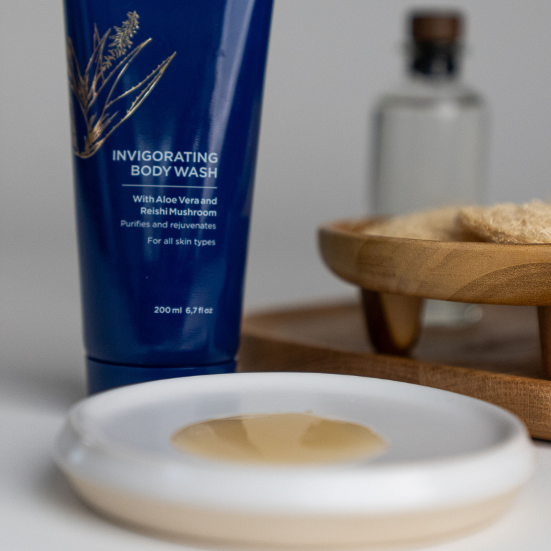 Curaloe invigorating body wash with a white soap dish containing soap on a neutral background