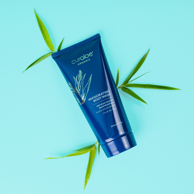 Curaloe Organic Invigorating Body Wash with green leaves on a light blue background