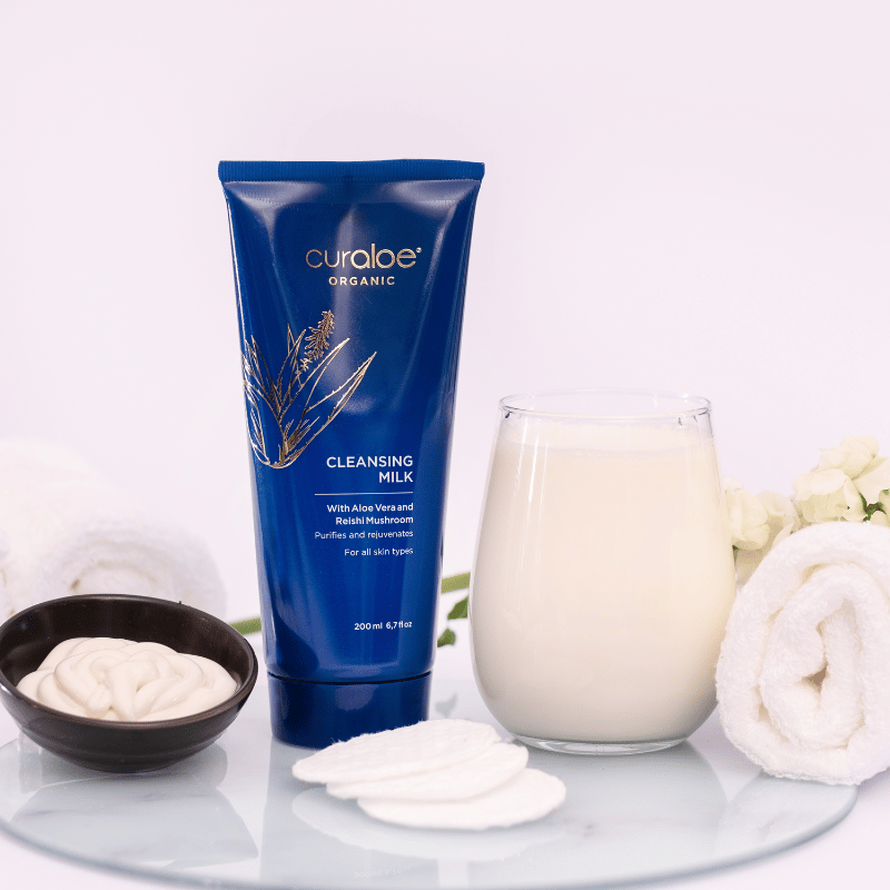 Curaloe Organic cleansing milk tube with a glass of milk and white flowers on a white background