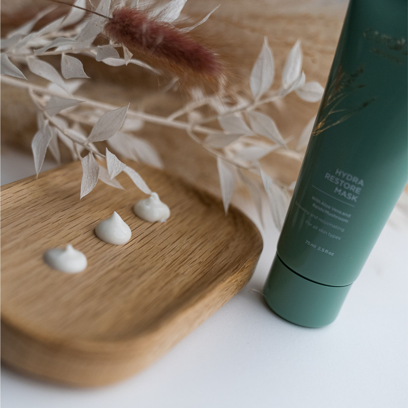 Curaloe Hydra Restore Mask with white cream on a wooden board and dried plants in the background