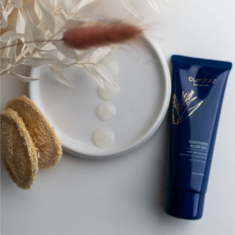 Curaloe Soothing Aloe Gel tube on a white surface with a white dish and natural elements.