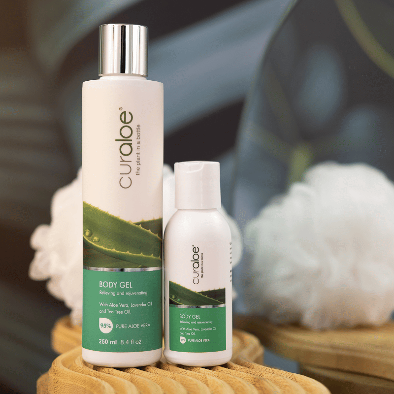 Curaloe body gel bottles on a textured surface with a blurred natural background
