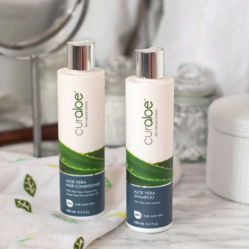 Two bottles of Curaloe Aloe Vera shampoo and conditioner on a bathroom counter.