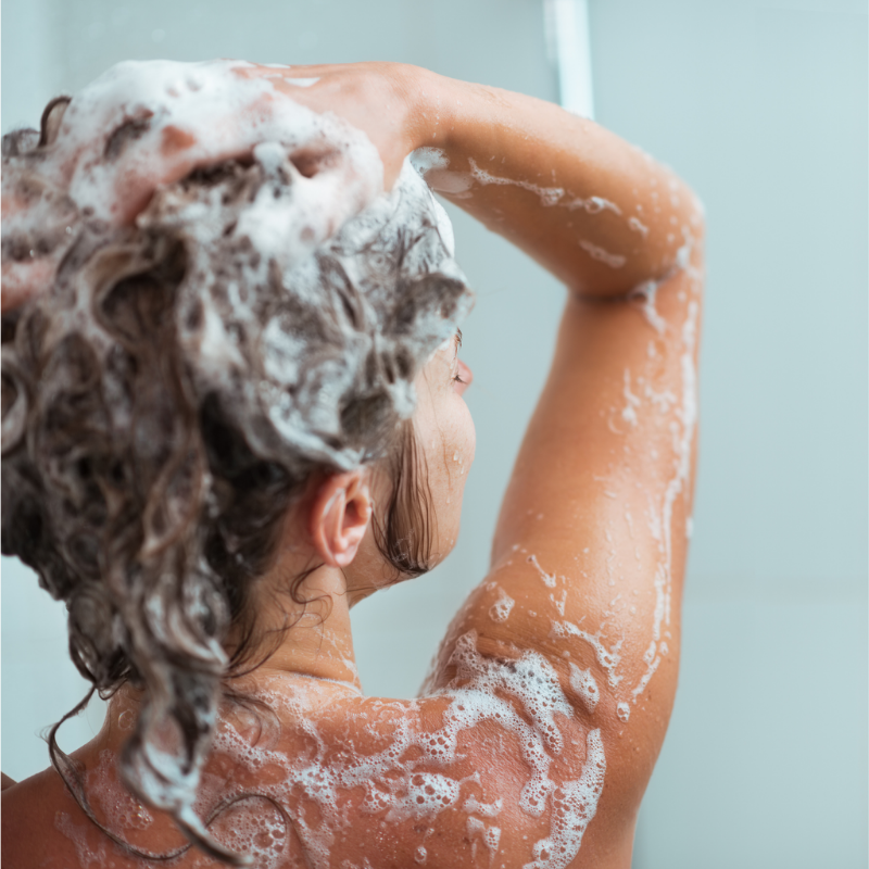Person with soapy hair and body, standing in a bathroom.
