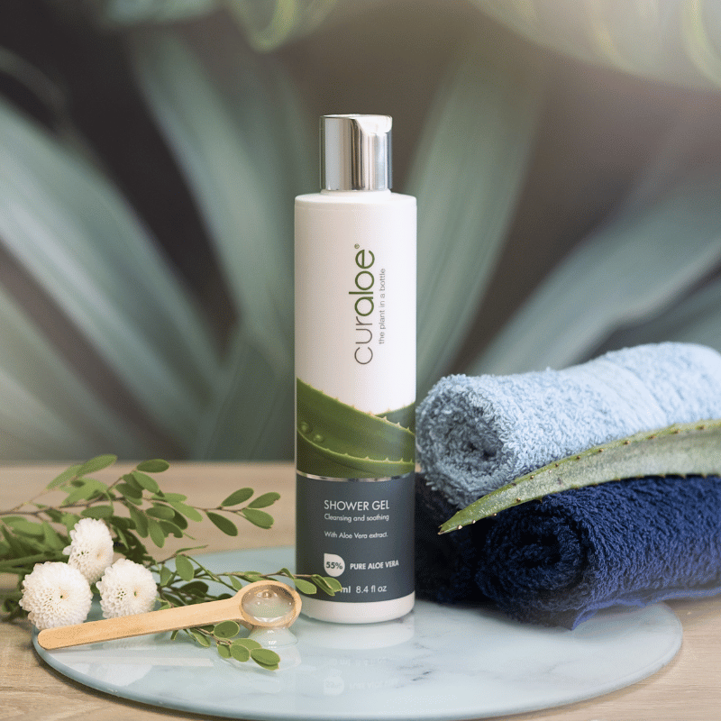 Curaloe shower gel bottle with towels and aloe vera leaf on a marble tray