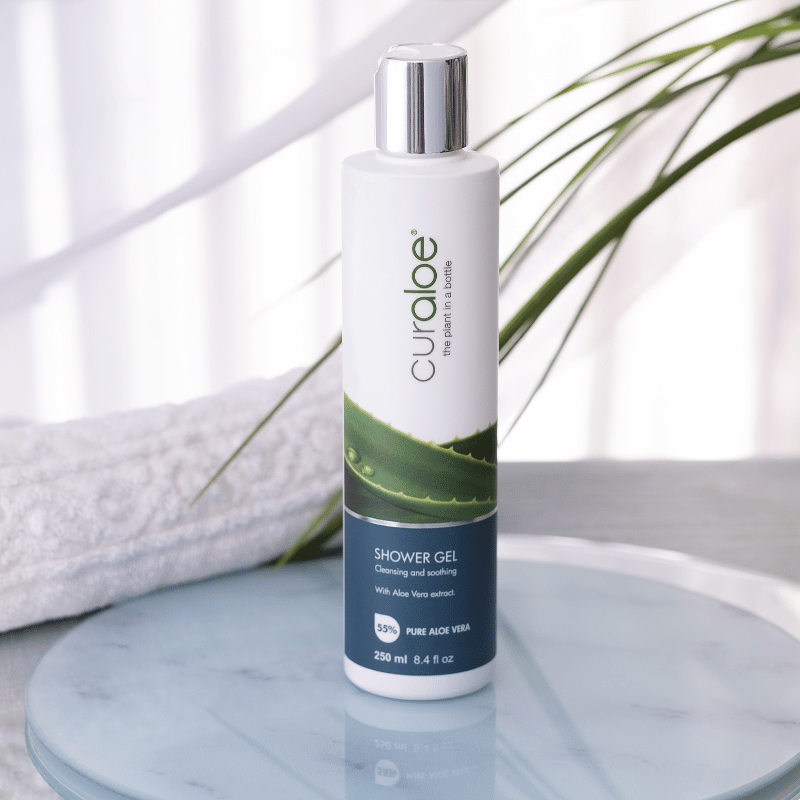 Curaloe shower gel bottle on a marble surface with a plant in the background