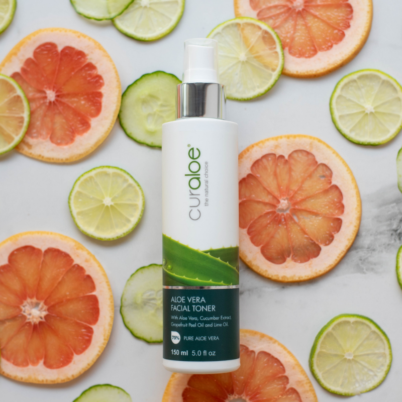 Curaloe aloe vera facial toner bottle surrounded by sliced citrus fruits on a white background