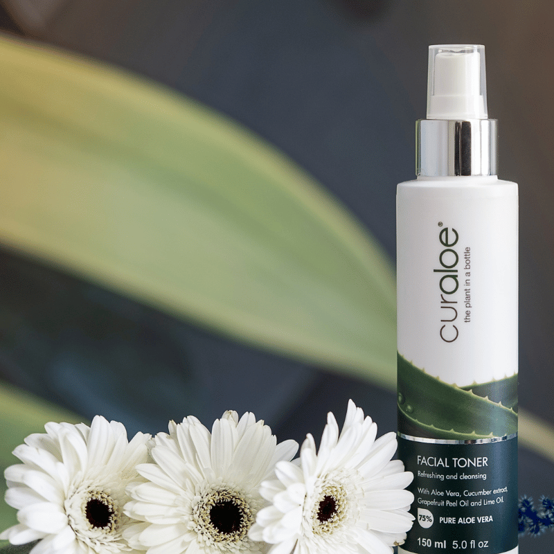 Curaloe facial toner bottle with white flowers on a blurred natural background