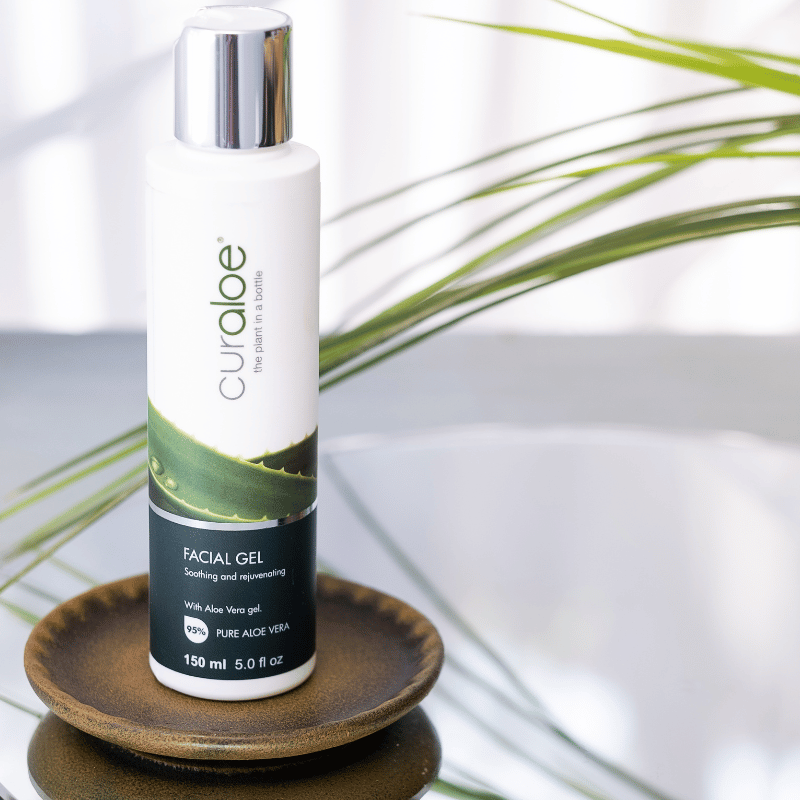 Curaloe facial gel bottle on a wooden coaster with a plant in the background