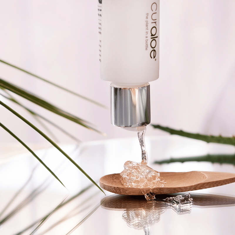 Curaloe product being dripped onto a wooden spoon with palm leaves in the background
