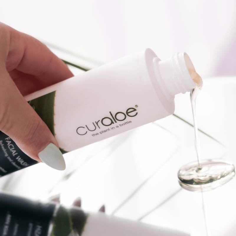 Hand holding a bottle of curaloe with dropper, white background