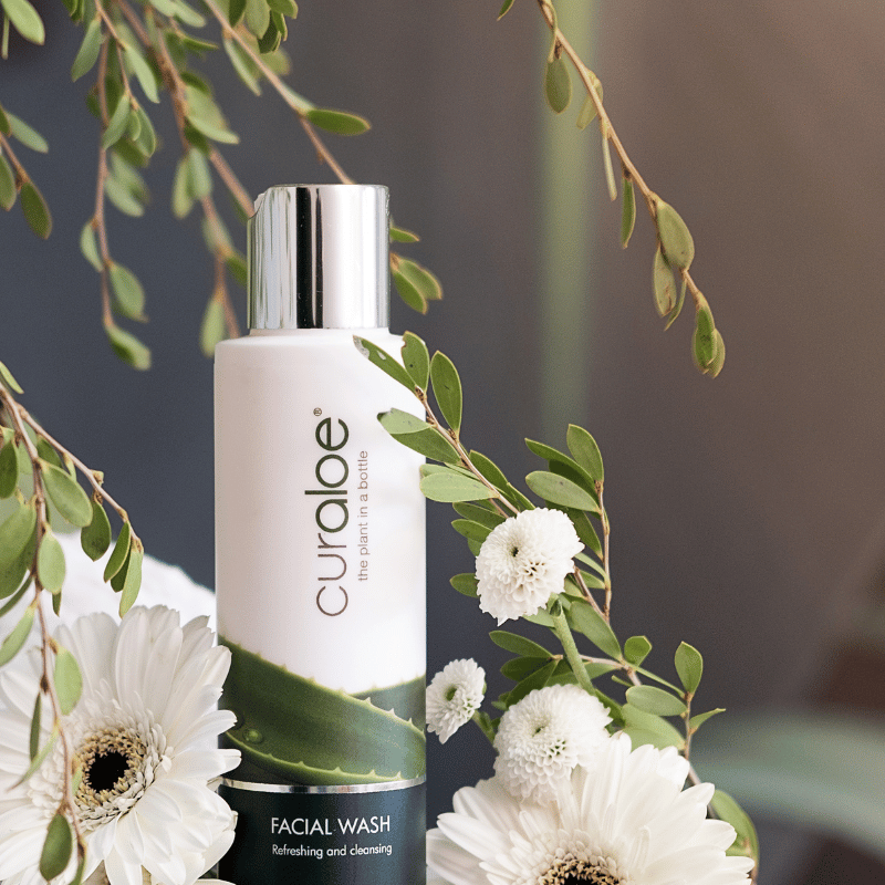 Curaloe facial wash bottle with green leaves and white flowers on a dark background