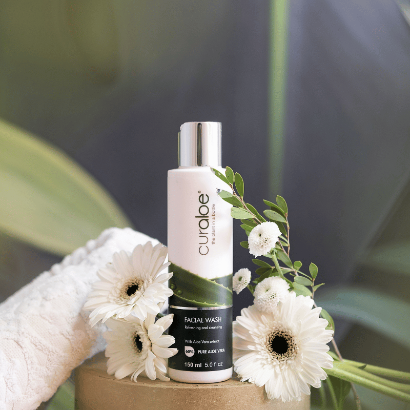 Curaloe facial wash bottle with flowers on a blurred natural background