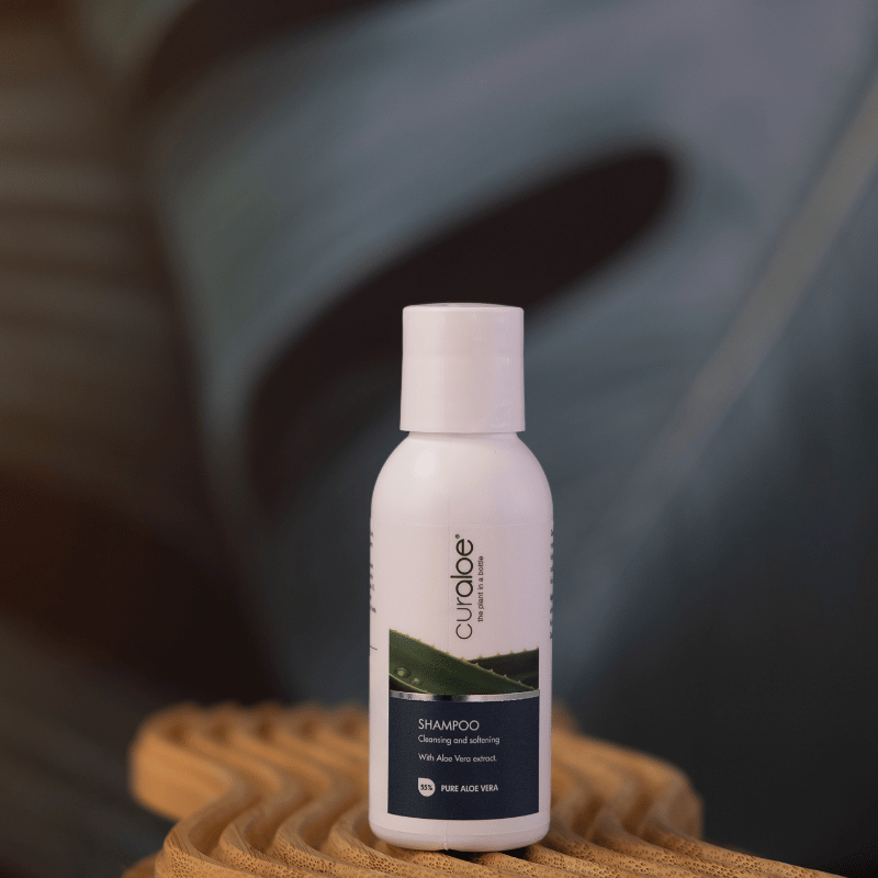Curaloe mini shampoo bottle on a textured surface with a blurred leaf background