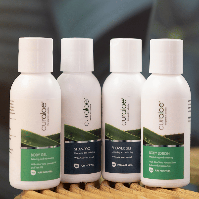 Four Curaloe skincare products on a wooden stand with a blurred background