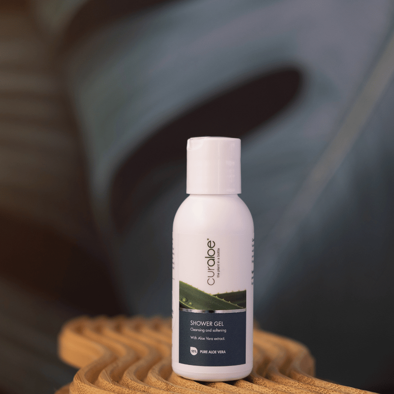 Curaloe shower gel on a woven surface with a blurred plant background