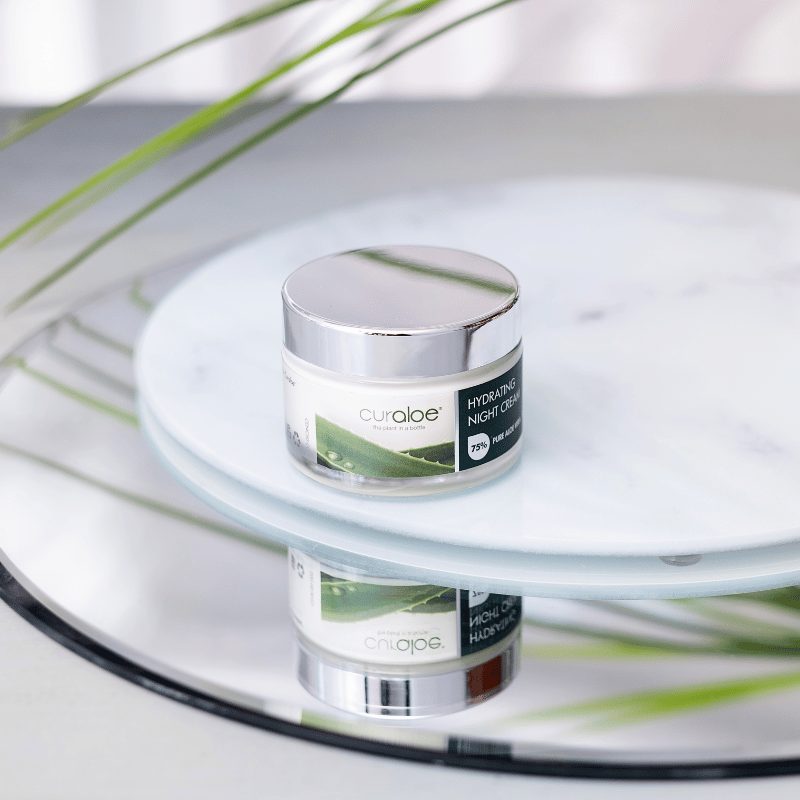 Curaloe Night Cream with blurred green leaves in the background