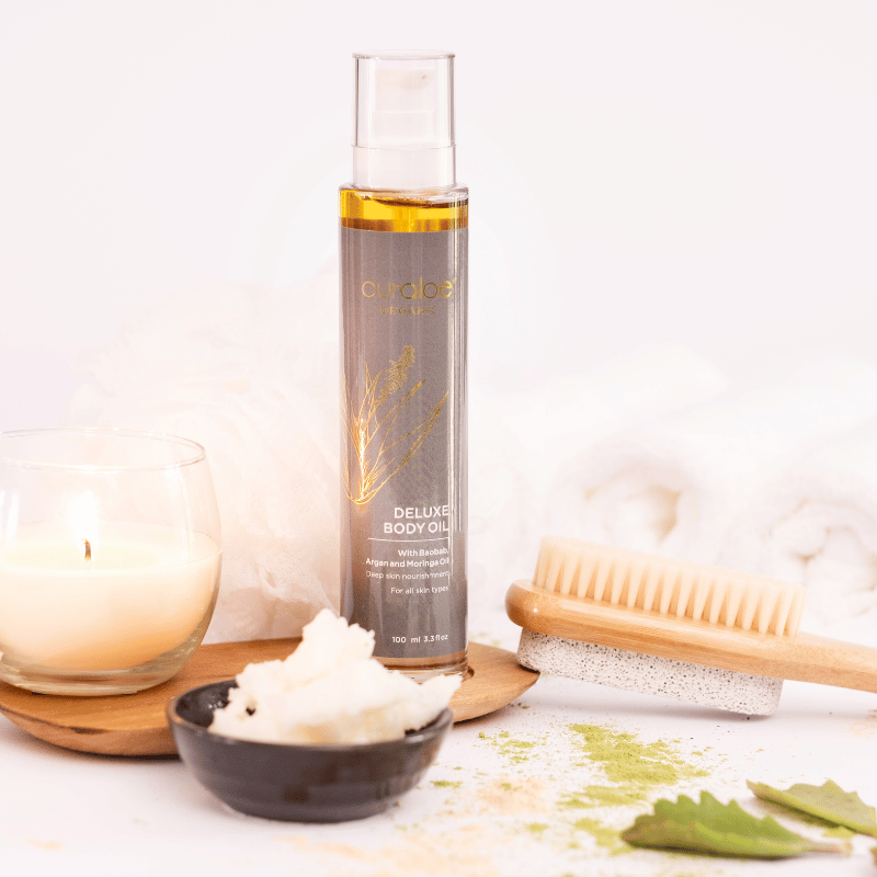 Curaloe Face & Body oil bottle with a candle, soap, and brush on a white background