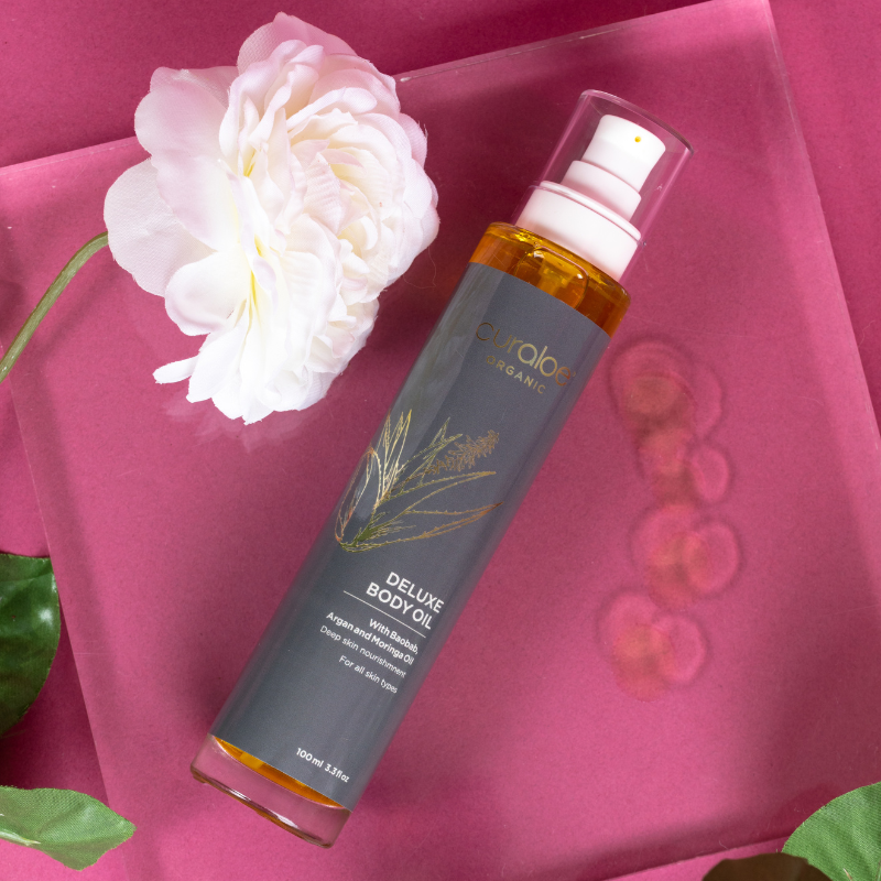 Curaloe Face & Body oil bottle with a white flower on a pink background