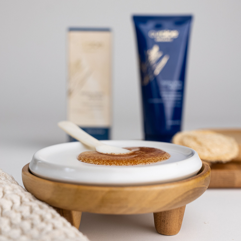 Ceramic dish with brown powder and white stick, surrounded by skincare products on a light background