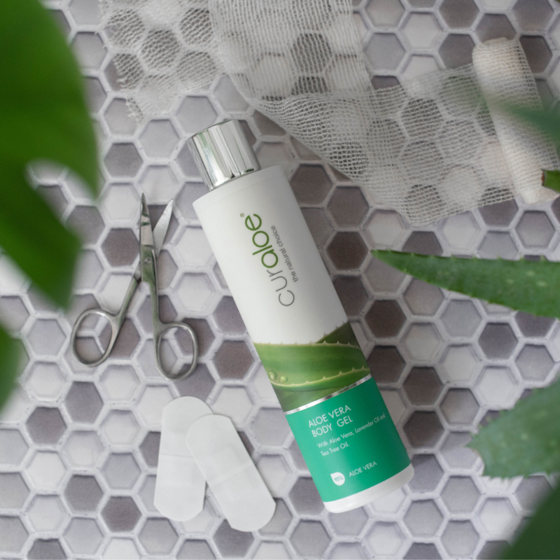 Curaloe Aloe Vera body gel bottle on a textured surface with scissors and aloe vera leaves.