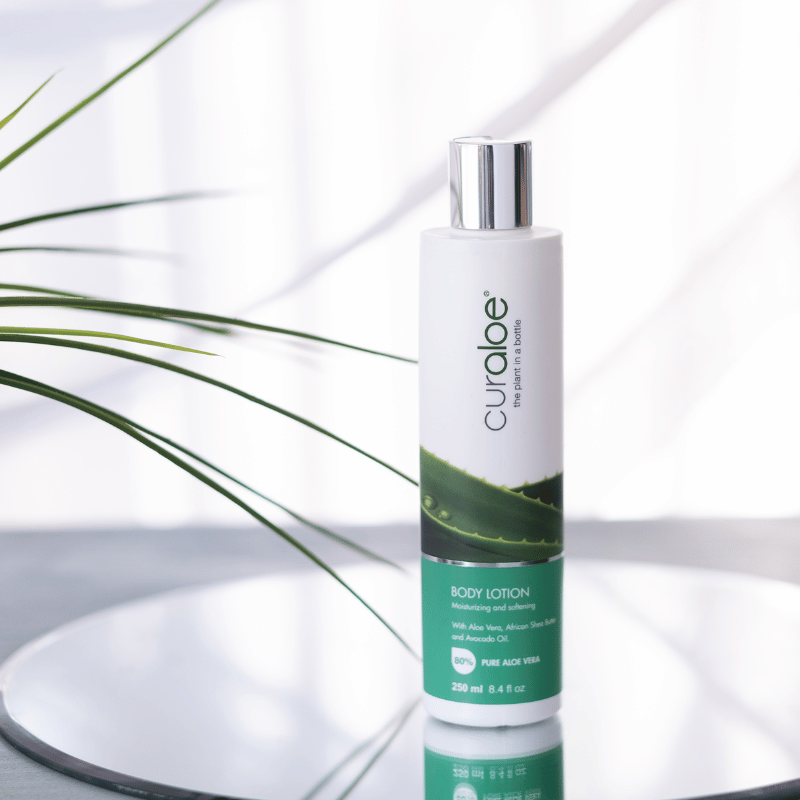 Curoloe body lotion bottle on a reflective surface with a plant leaf in the background