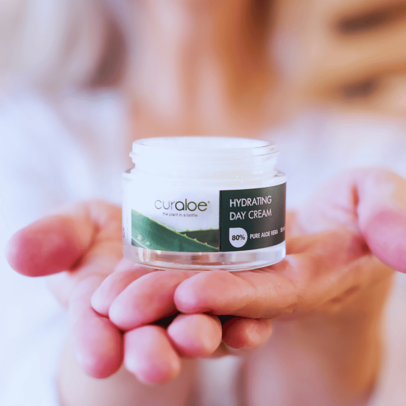 Hand holding a jar of Curaloe hydrating day cream with a blurred background